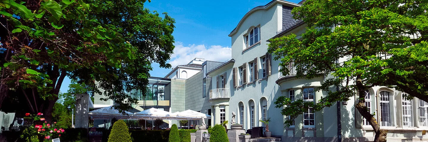 Opelvilla in Rüsselsheim mit grünem Garten bei blauem Himmel.