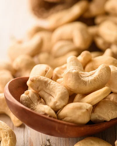 Naturbelassene Cashewkerne liegen in einem Holzlöffel und auf einem Tisch.