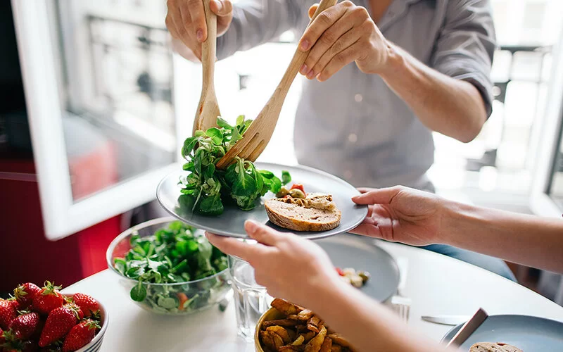 Eine Person platziert mit einem Holzbesteck Salat auf einen Teller.