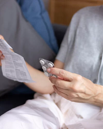 Eine nicht erkennbare Frau hält in einer Hand eine Blisterpackung mit Tabletten und in der anderen einen Beipackzettel.