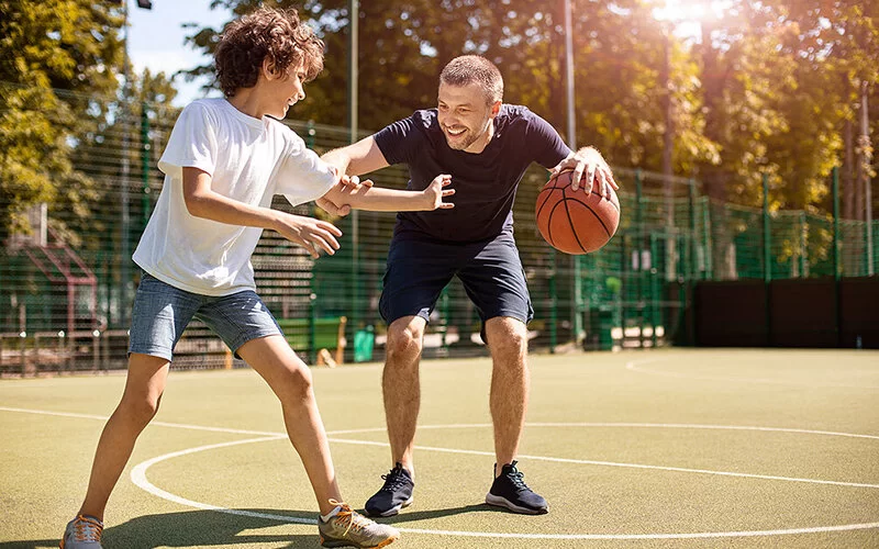 Ein Mann spielt mit einem Jungen auf einem Basketballplatz im Freien Basketball.