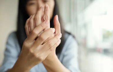 Im Vordergrund die Hände einer Frau, die sich die Innenfläche ihrer linken Hand ansieht.