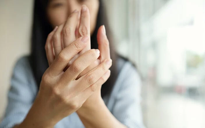 Im Vordergrund die Hände einer Frau, die sich die Innenfläche ihrer linken Hand ansieht.