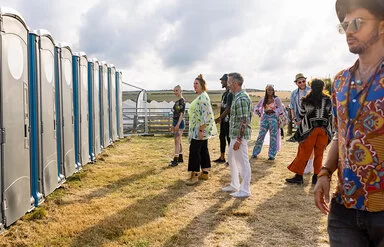 Menschen stehen vor mobilen Toiletten auf einem Festival und warten in der Schlange.