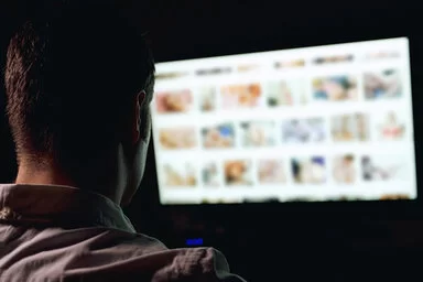 Ein Mann, der unter Sexsucht leidet, sitzt vor einem Bildschirm und schaut Pornos.