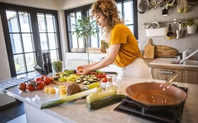 Eine Frau verarbeitet in der Küche gesunde Lebensmittel wie Tomaten und Brokkoli.