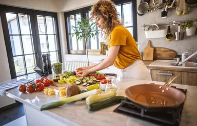 Eine Frau verarbeitet in der Küche gesunde Lebensmittel wie Tomaten und Brokkoli.