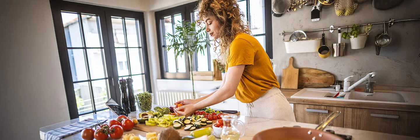 Eine Frau verarbeitet in der Küche gesunde Lebensmittel wie Tomaten und Brokkoli.