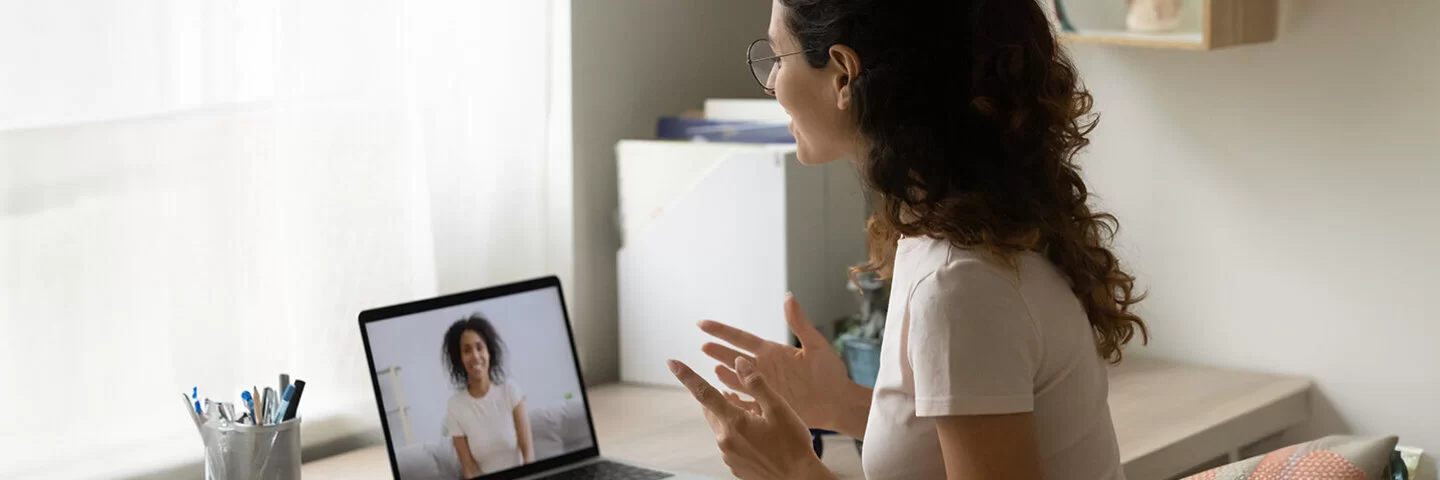 Zu sehen ist eine Frau mit Brille von der Seite, die über ihren Laptop mit einer Psychotherapeutin spricht.