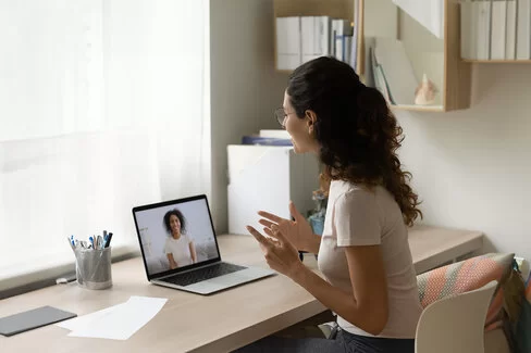 Zu sehen ist eine Frau mit Brille von der Seite, die über ihren Laptop mit einer Psychotherapeutin spricht.