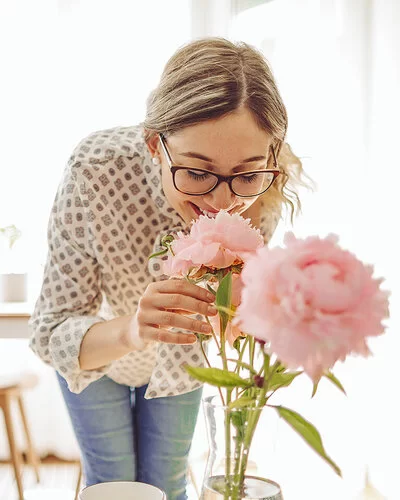 Eine Frau riecht an rosa Pfingstrosen in einer Vase und genießt den Duft der Blumen.