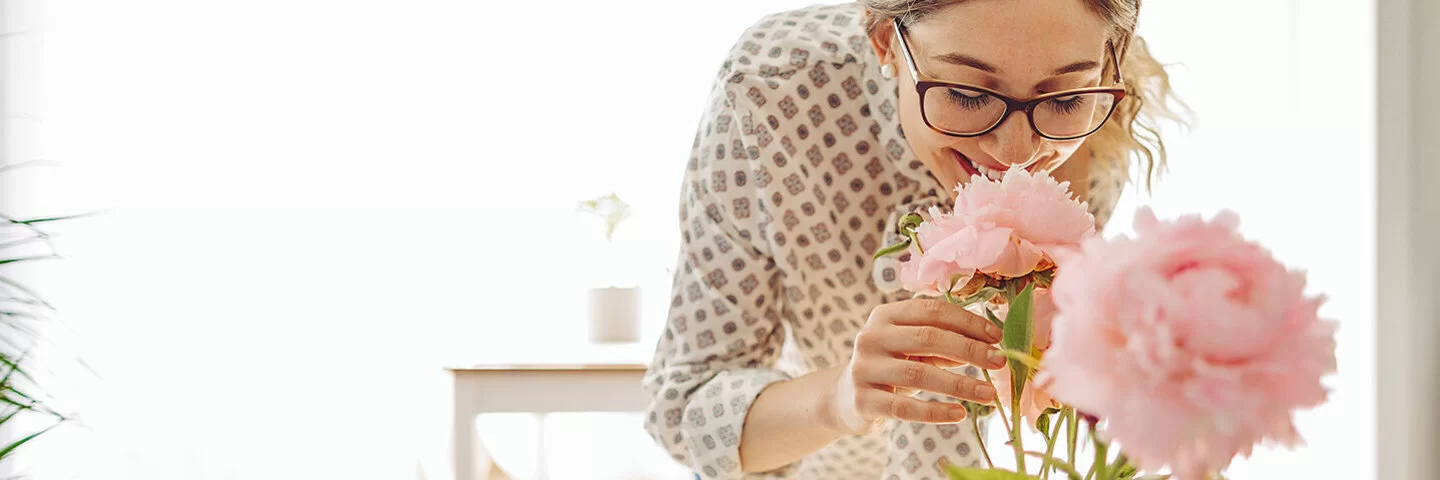 Eine Frau riecht an rosa Pfingstrosen in einer Vase und genießt den Duft der Blumen.