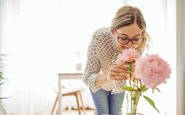 Eine Frau riecht an rosa Pfingstrosen in einer Vase und genießt den Duft der Blumen.