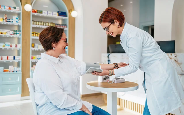 Eine junge Apothekerin misst in einer Apotheke den Blutdruck einer Kundin.