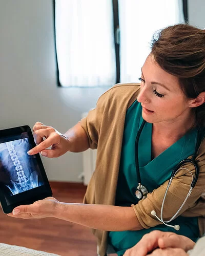 Eine Ärztin erklärt einer Patientin anhand eines Röntgenbildes auf einem Bildschirm die Ergebnisse der Knochendichtemessung.