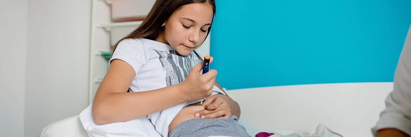 Ein junges Mädchen mit Typ-1-Diabetes sitzt auf einem Sofa und spritzt sich mit einem Insulinpen eine Dosis Insulin in den Bauch.