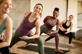 Mehrere Frauen trainieren zusammen in einem Yoga-Kurs. Sie stehen in einer Yoga-Haltung auf ihren Matten.