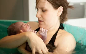 Junge Mutter hält ihr Neugeborenes nach einer Wassergeburt im Arm.