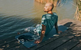 Ein Mann führt auf seiner Yogamatte am Wasser eine Achtsamkeitsübung zur Krebsbewältigung durch.