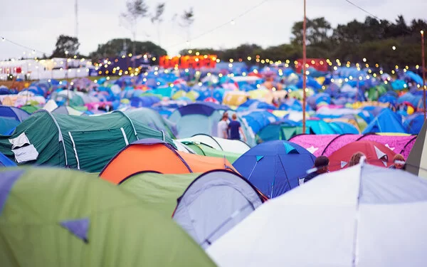 Aufnahme eines Campingplatzes mit vielen bunten Zeltdächern auf einem Outdoor-Festival. Über den Zelten hängen Lichterketten.