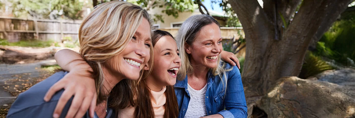 Ein Mädchen sitzt zwischen zwei älteren Frauen, alle lachen gemeinsam.