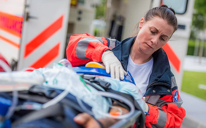 Eine Rettungssanitäterin kümmert sich um eine Person, die auf einer Trage liegt.