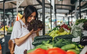 Junge Frau riecht an einem Salat auf einem Markt mit viel Gemüse. Bildunterschrift: Frisches Gemüse vom Markt ist Balsam für die Seele.