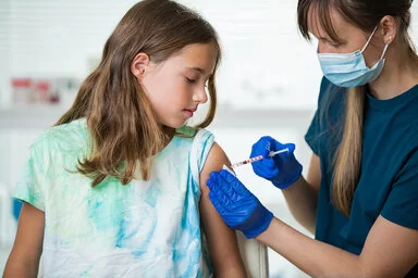 Etwa 11-jähriges Mädchen erhält eine Impfung in den linken Oberarm.