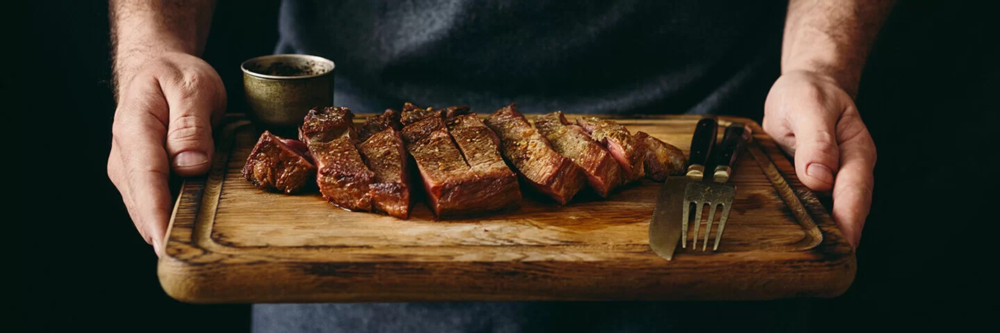 Ein Mann hält ein Schneidebrett mit einem gegrillten und in Scheiben geschnittenen Rindersteak.