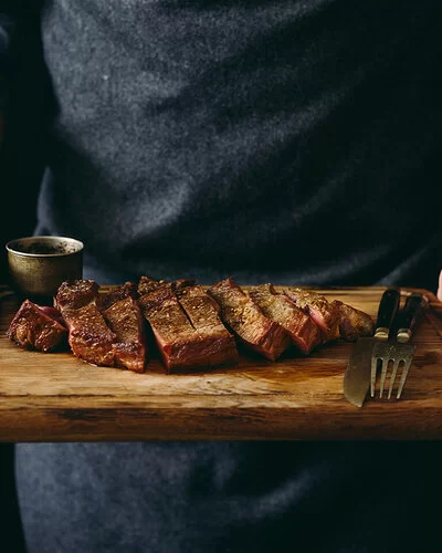 Ein Mann hält ein Schneidebrett mit einem gegrillten und in Scheiben geschnittenen Rindersteak.