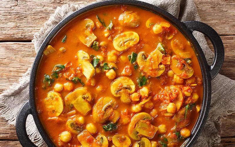 Vegane indische Pilzcurry mit Spinat, Tomaten und Kichererbsen in einem gusseisernen Topf.