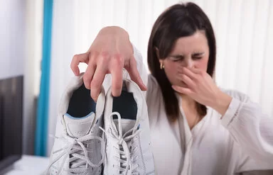 Eine Frau hält sich mit einer Hand die Nase zu und mit der anderen ein Paar Sportschuhe nach vorne.