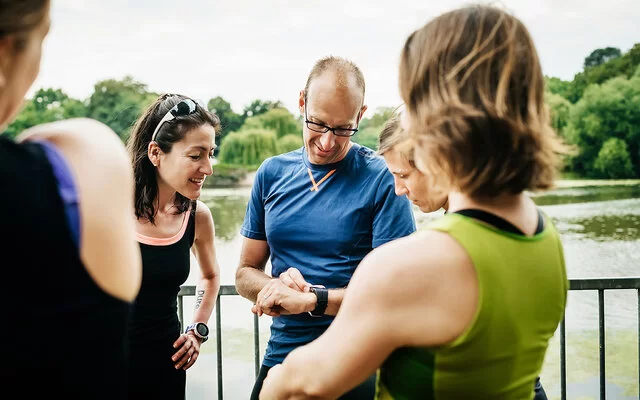 Eine Gruppe Frauen steht um einen Mann herum, der auf seine Smartwatch sieht.