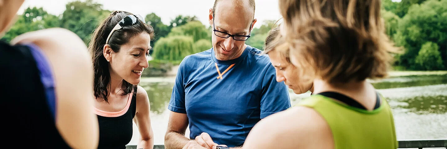 Eine Gruppe Frauen steht um einen Mann herum, der auf seine Smartwatch sieht.