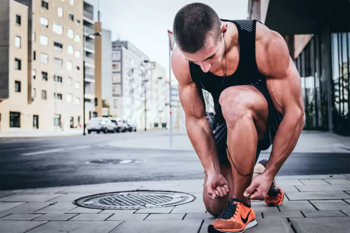 Ein muskulöser junger Sportler bindet sich die Schnürsenkel vor einem Lauf.