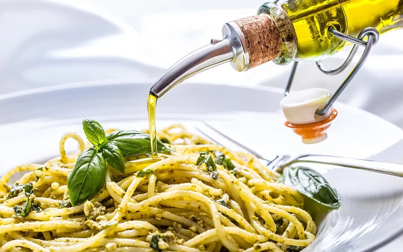 Jemand gießt Olivenöl auf seine gekochten Spaghetti.