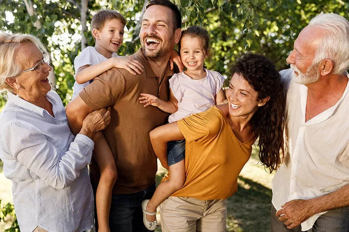 Eine Familie mit Eltern, Großeltern und Kindern steht glücklich im Garten. 