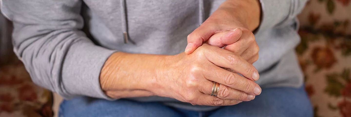 Eine Frau in sitzender Position umschließt mit einer Hand den Daumen der anderen Hand.