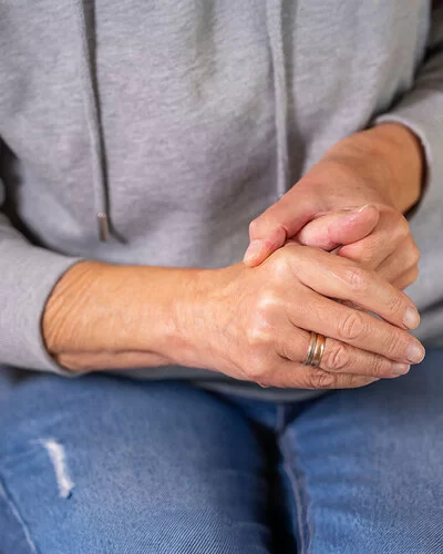 Eine Frau in sitzender Position umschließt mit einer Hand den Daumen der anderen Hand.