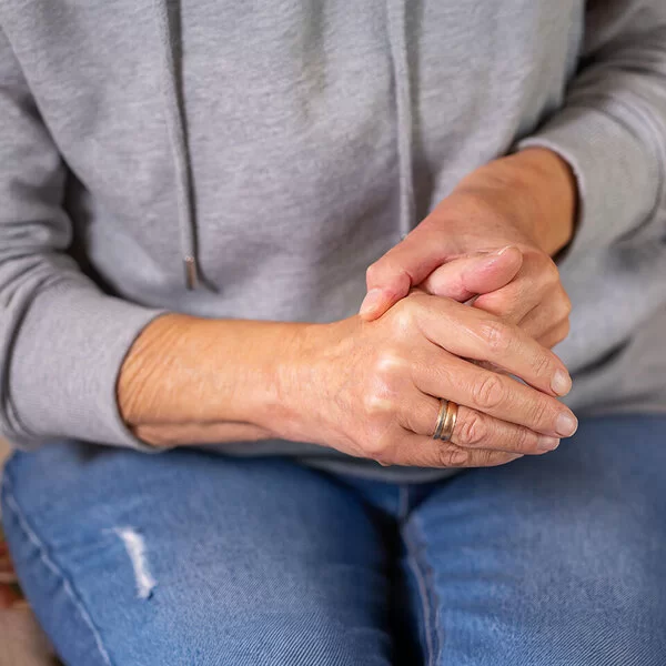 Eine Frau in sitzender Position umschließt mit einer Hand den Daumen der anderen Hand.