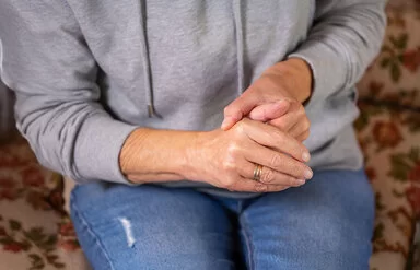 Eine Frau in sitzender Position umschließt mit einer Hand den Daumen der anderen Hand.