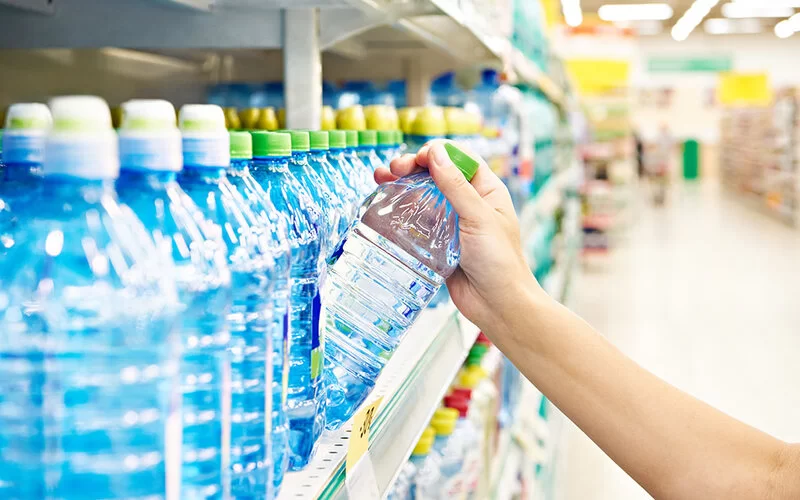 Eine Hand greift nach einer Wasserflasche, die in einem Supermarktregal steht.