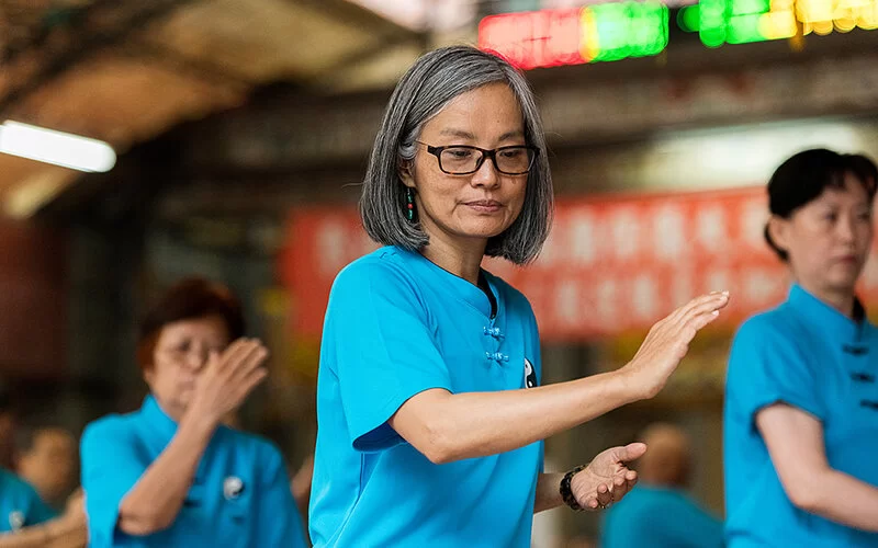 Drei Asiatinnen führen traditionelle Tai Chi Übungen durch.