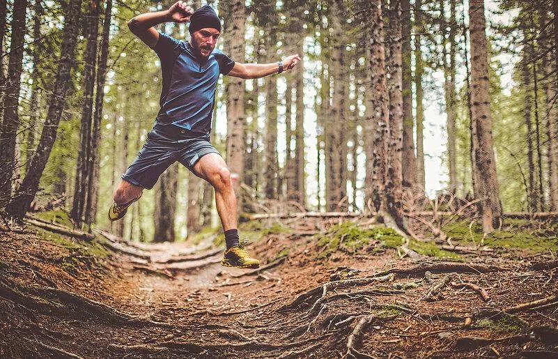 Eine männliche Person in Sportkleidung läuft einen Trail in einem Wald.
