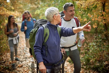 Eine Gruppe von fünf Menschen mit Rucksäcken wandert durch einen herbstlichen Wald.