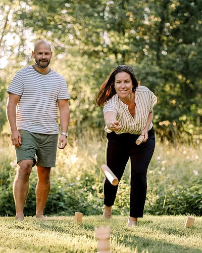 Eine Frau wirft mit einem Wurfholz auf Holzklötze, die auf einer Wiese stehen.