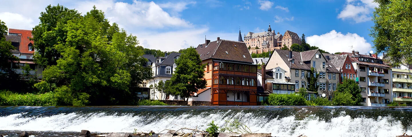 Marburg mit der Lahn im Vorder- und Schloss Marburg im Hintergrund.