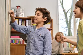 Ein Junge schreibt mit einem Stück Kreide etwas an eine Tafel. „Science Kids: Gesundheit entdecken“ regt den Entdeckergeist der Kinder in Sachen Gesundheit an.