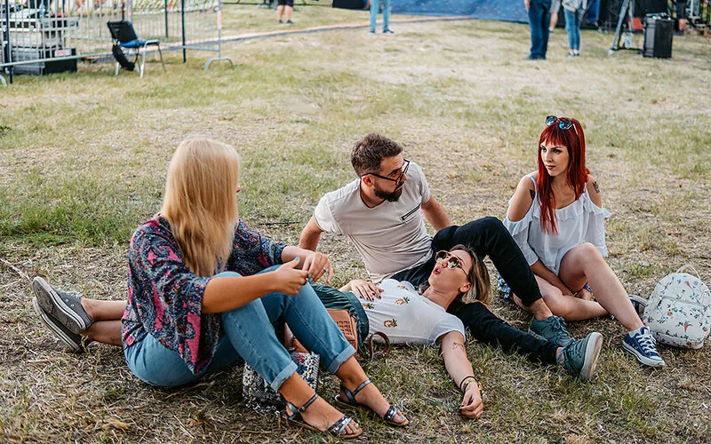 Eine Gruppe von vier Freunden sitzt und liegt zusammen auf dem Gelände eines Musikfestivals und unterhält sich.