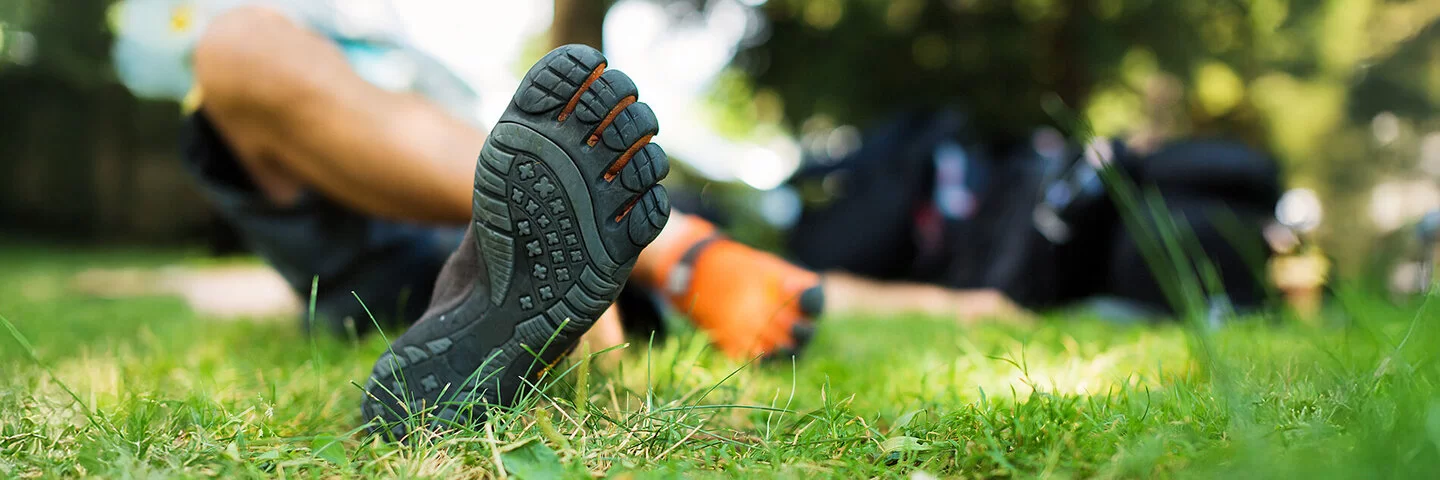 Eine Person liegt mit Barfußschuhen im Gras.